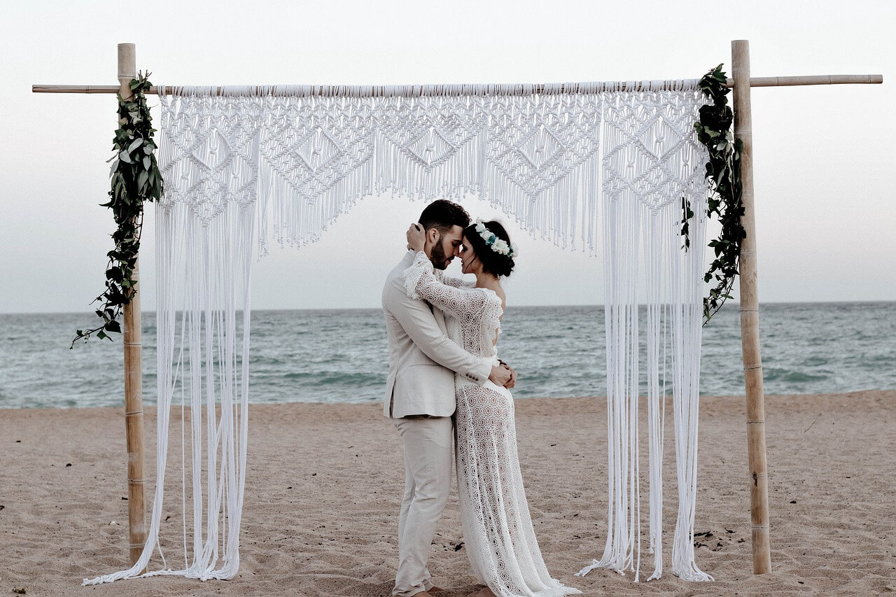 couple embracing in front of woven wedding backdrop on the beach
