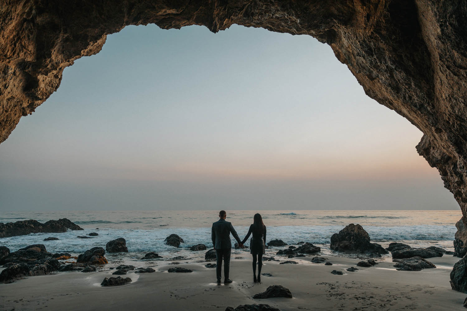 couple holding hands under a cave at the beach