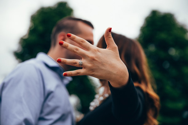 selective focus of couple kissing as woman holds engagement ring toward camera