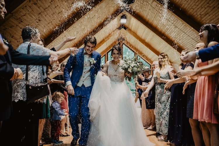 married couple walking down aisle as guests toss rice over them