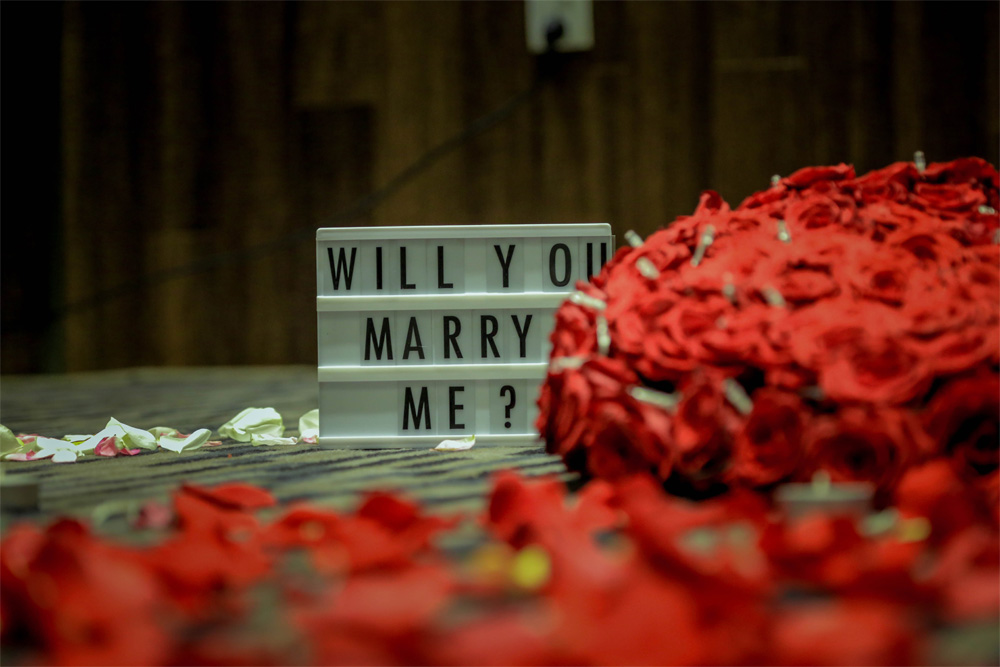 a selective focus image of a “will you marry me? sign with roses