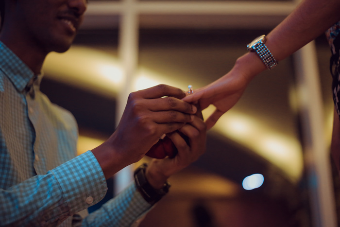 selective focus man kneeling putting engagement ring on woman’s hand