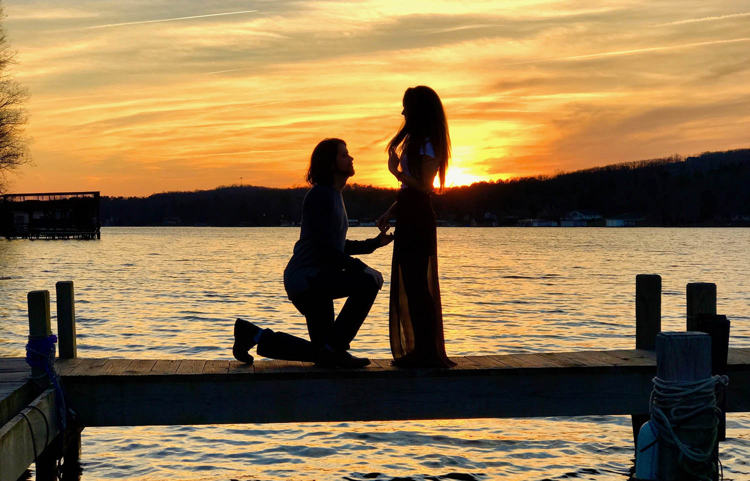 man proposing to woman on a dock while the sun is setting