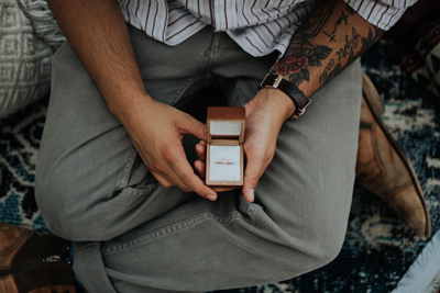 top view of man holding open engagement ring box in his lap